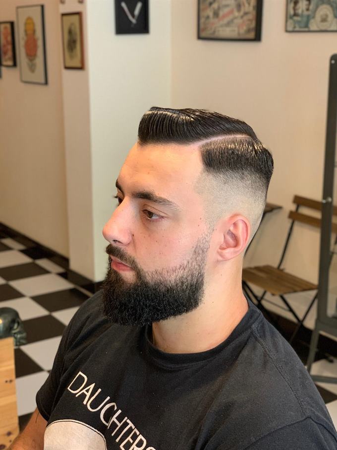 Corte com risco lateral e degradê, barba aparada — de perfil