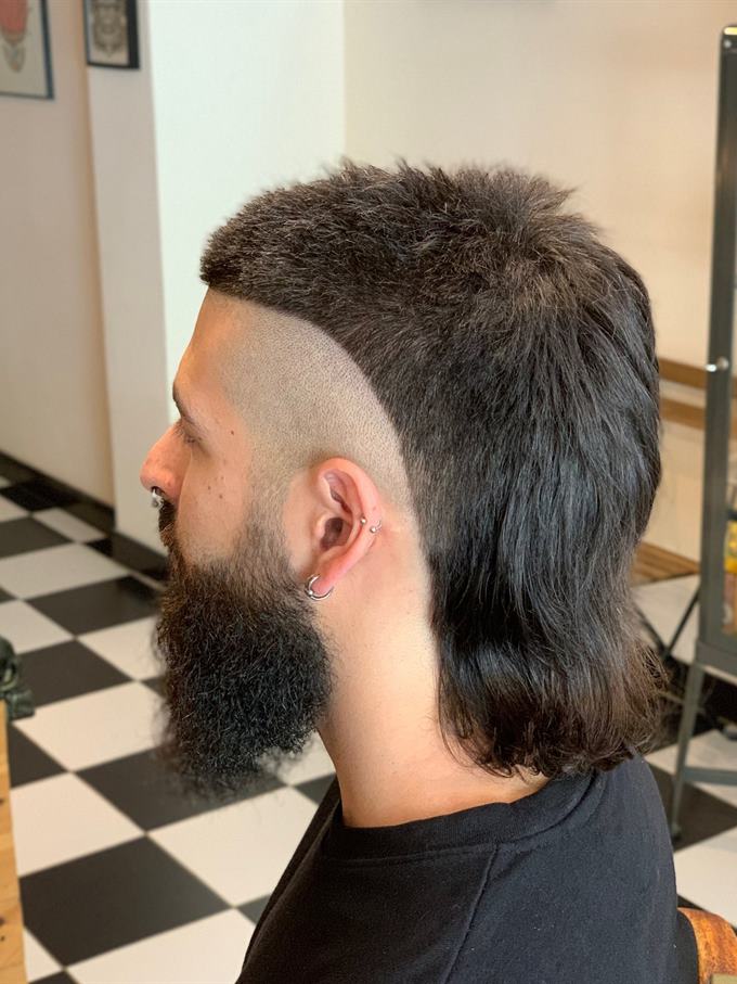 Mullet com laterais rapadas e barba cheia — de perfil